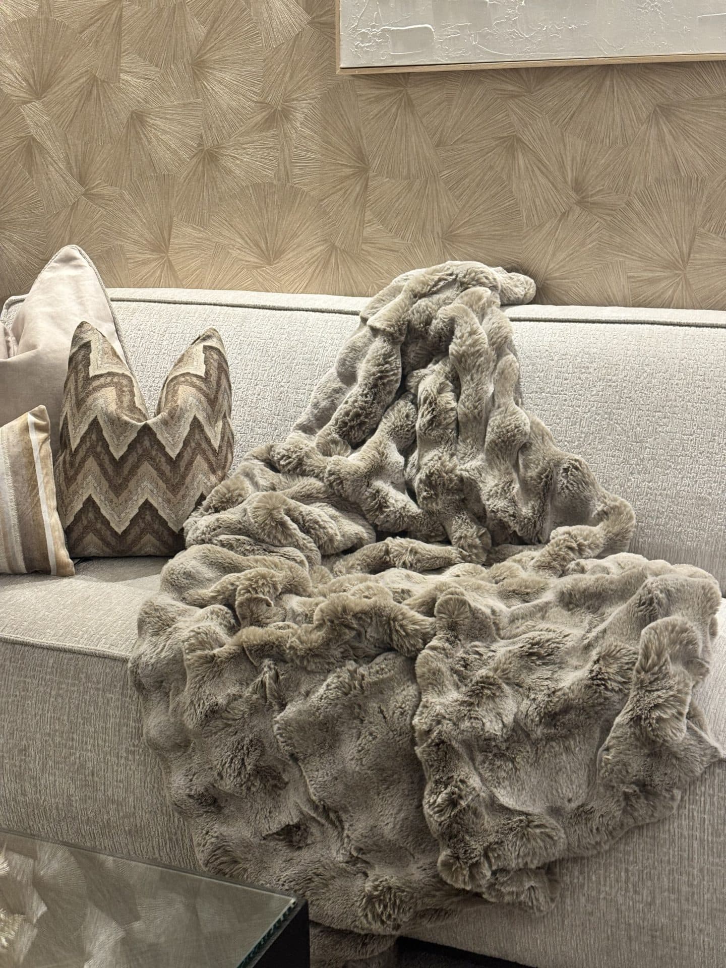 Wollige taupe plaid losjes over een lichte bank met gedessineerde kussens