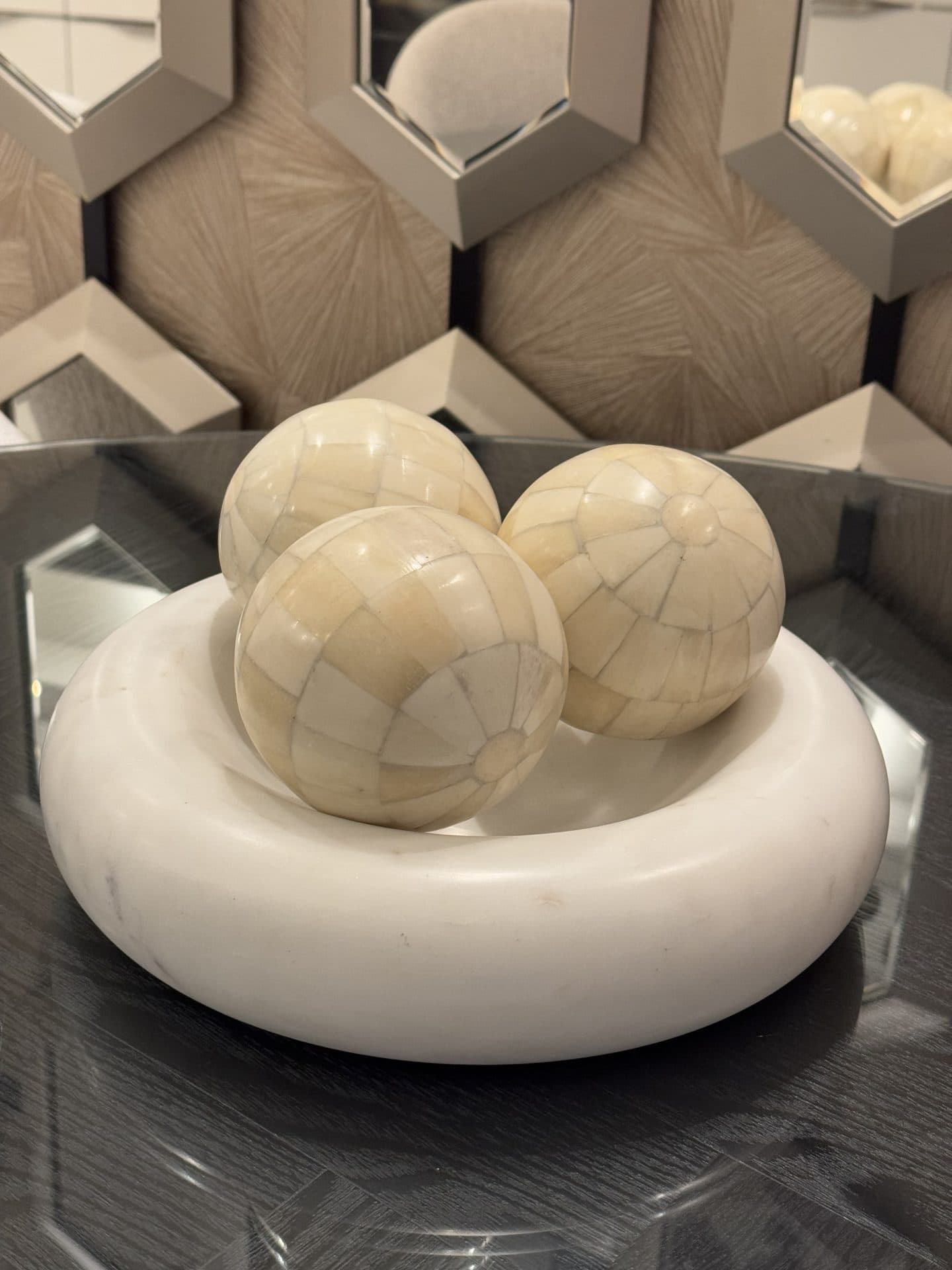 Ronde witte marmeren schaal met drie beige decoratieballen erin, op een glazen tafelblad