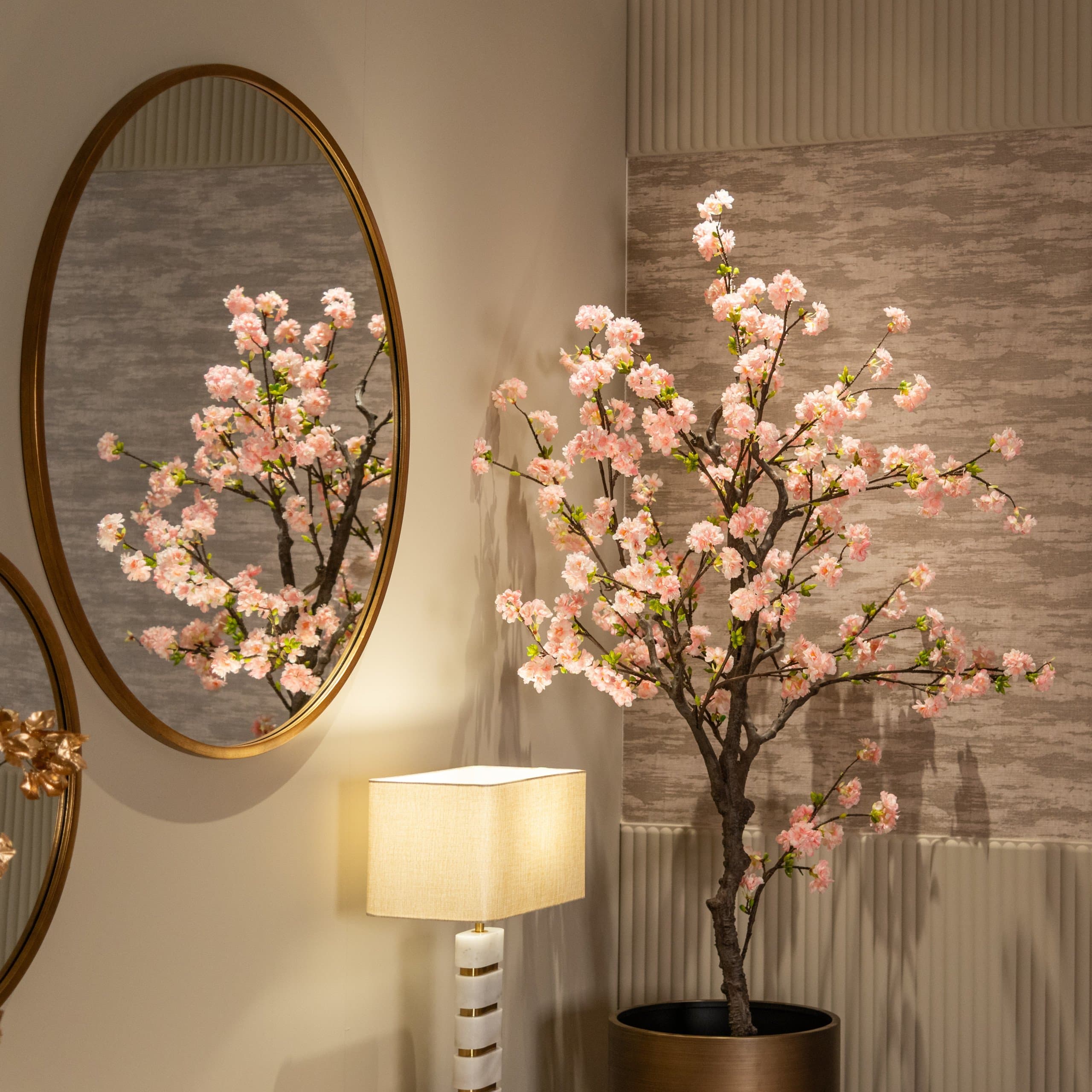 Ronde gouden wandspiegel naast een bloesemboom, met de takken weerspiegeld in het glas