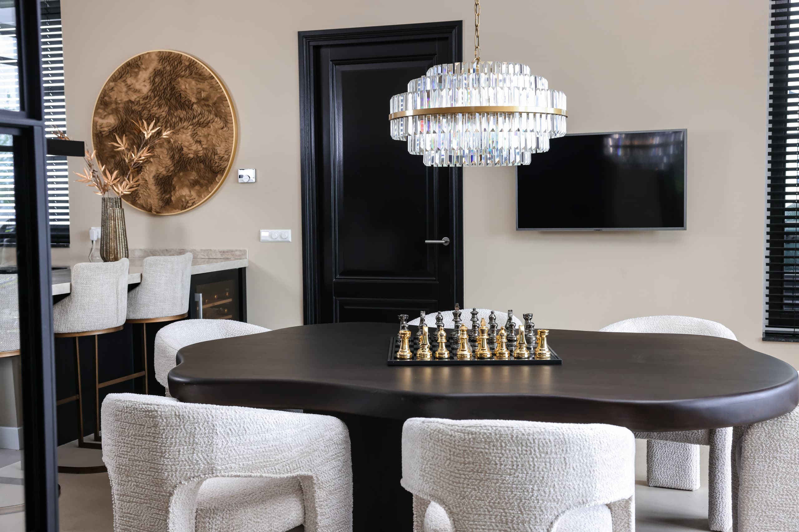 Donkere houten eettafel met organische vorm, crèmekleurige bouclé stoelen en een kristallen hanglamp in een eetkamer