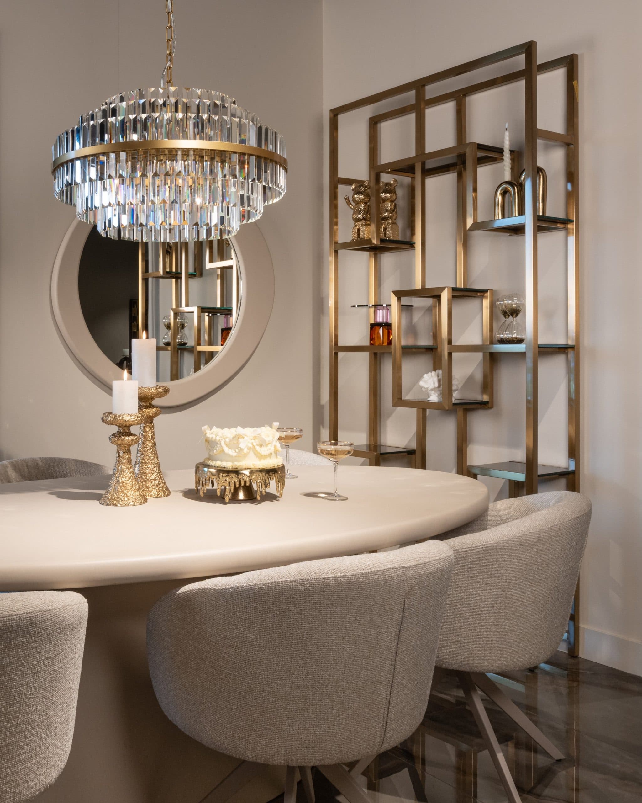 Ovale spiegel met brede beige lijst aan de wand boven een ronde eettafel met twee gouden kandelaars en een taart