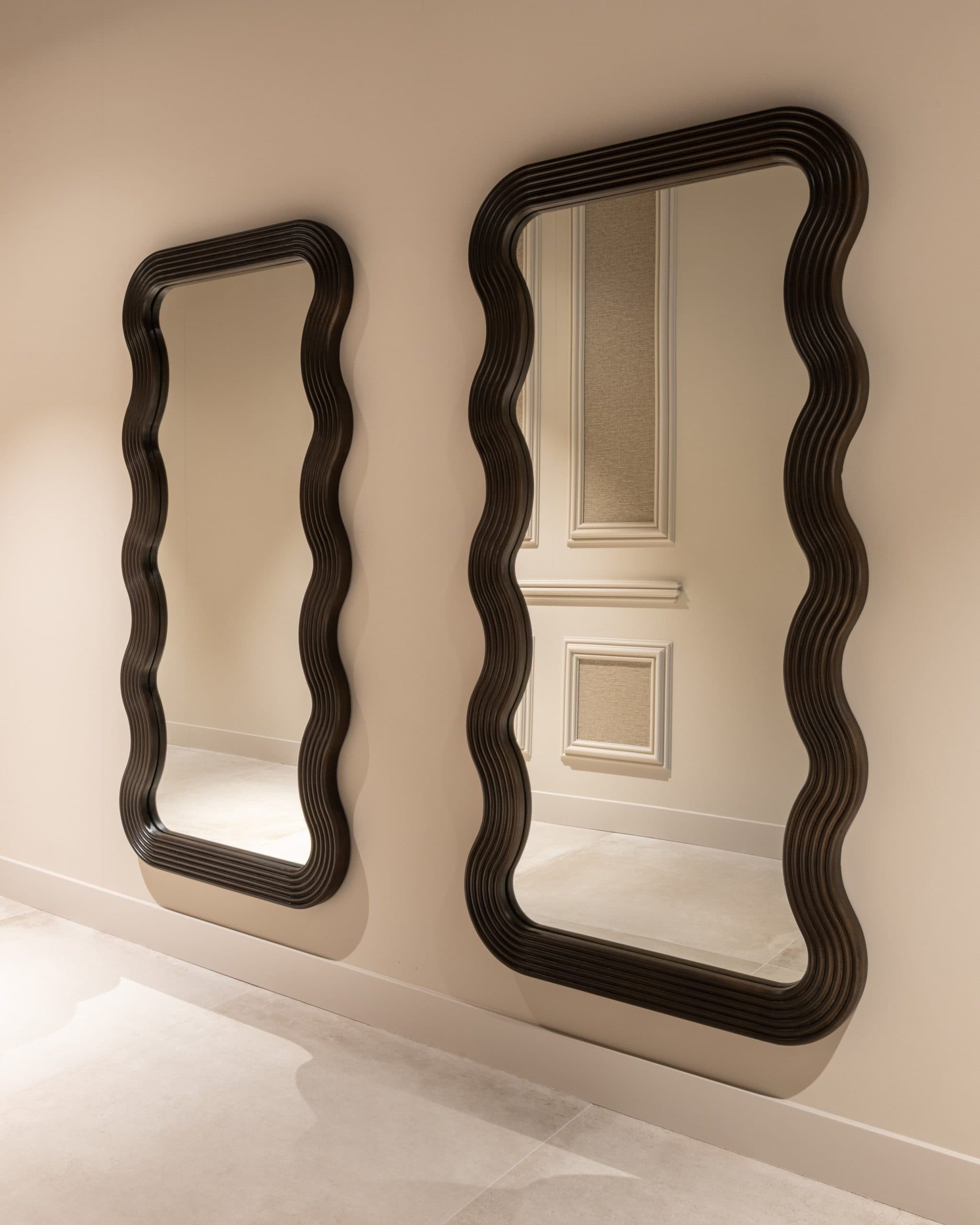 Twee hoge spiegels met golvend donkerbruin houten frame tegen een crèmekleurige wand met paneellijsten