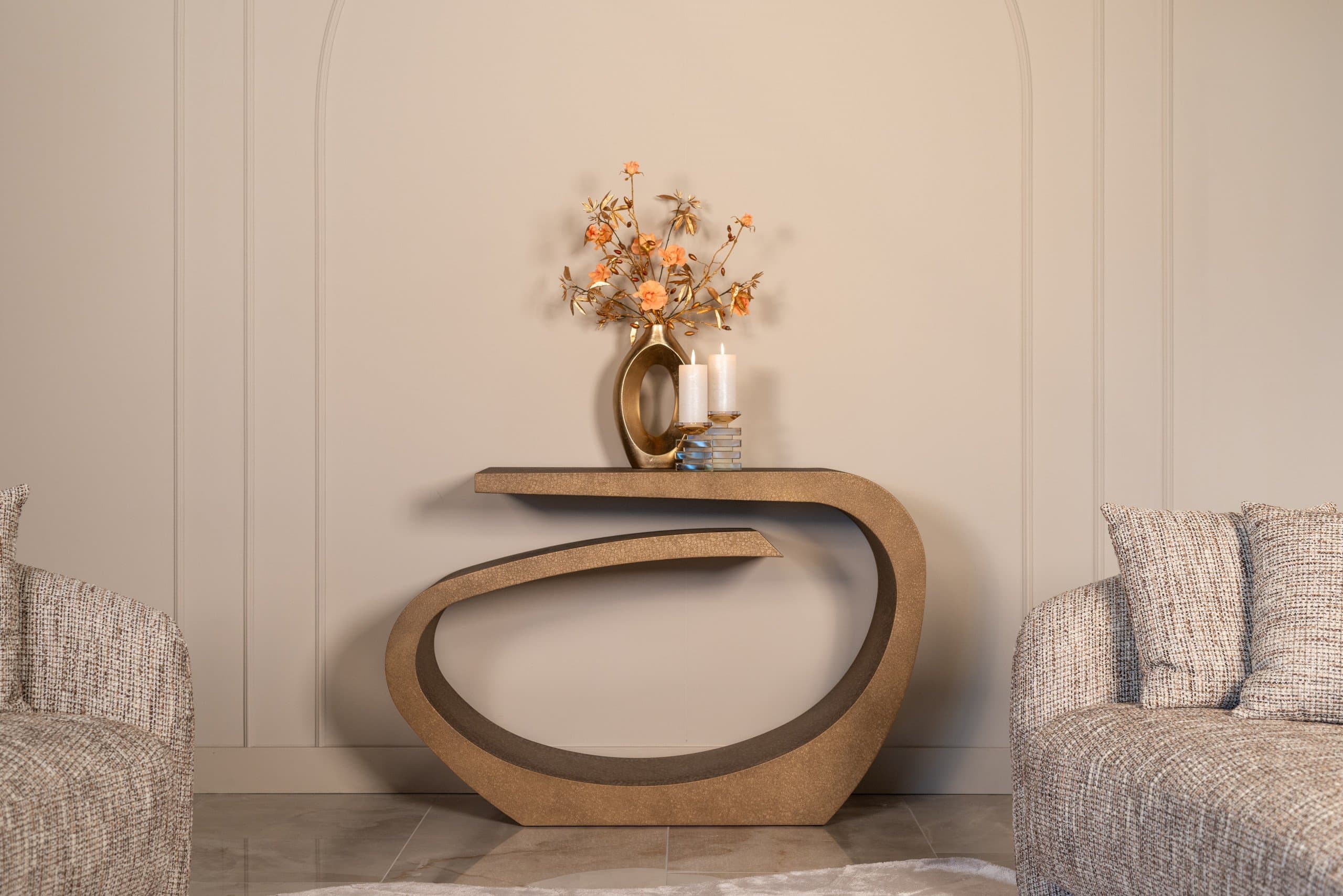 Goudkleurige console met gebogen vorm tegen een lichte lambriseringswand, met een vaas met oranje bloemen en twee kaarsen erop