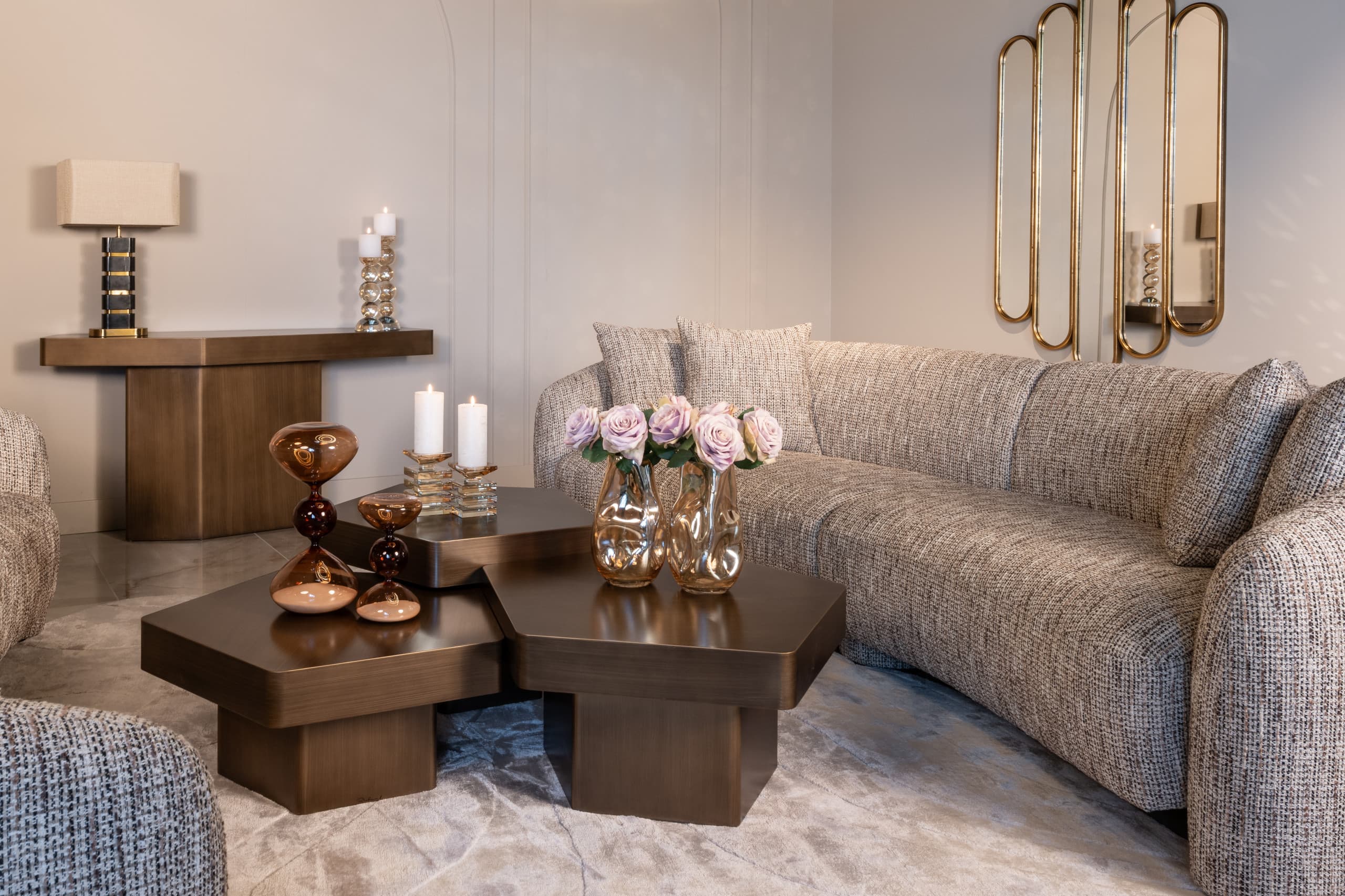 Warm verlichte ruimte met een brandende tafellamp op een houten console, kaarsen op een lage tafel en een goudkleurig wandobject.