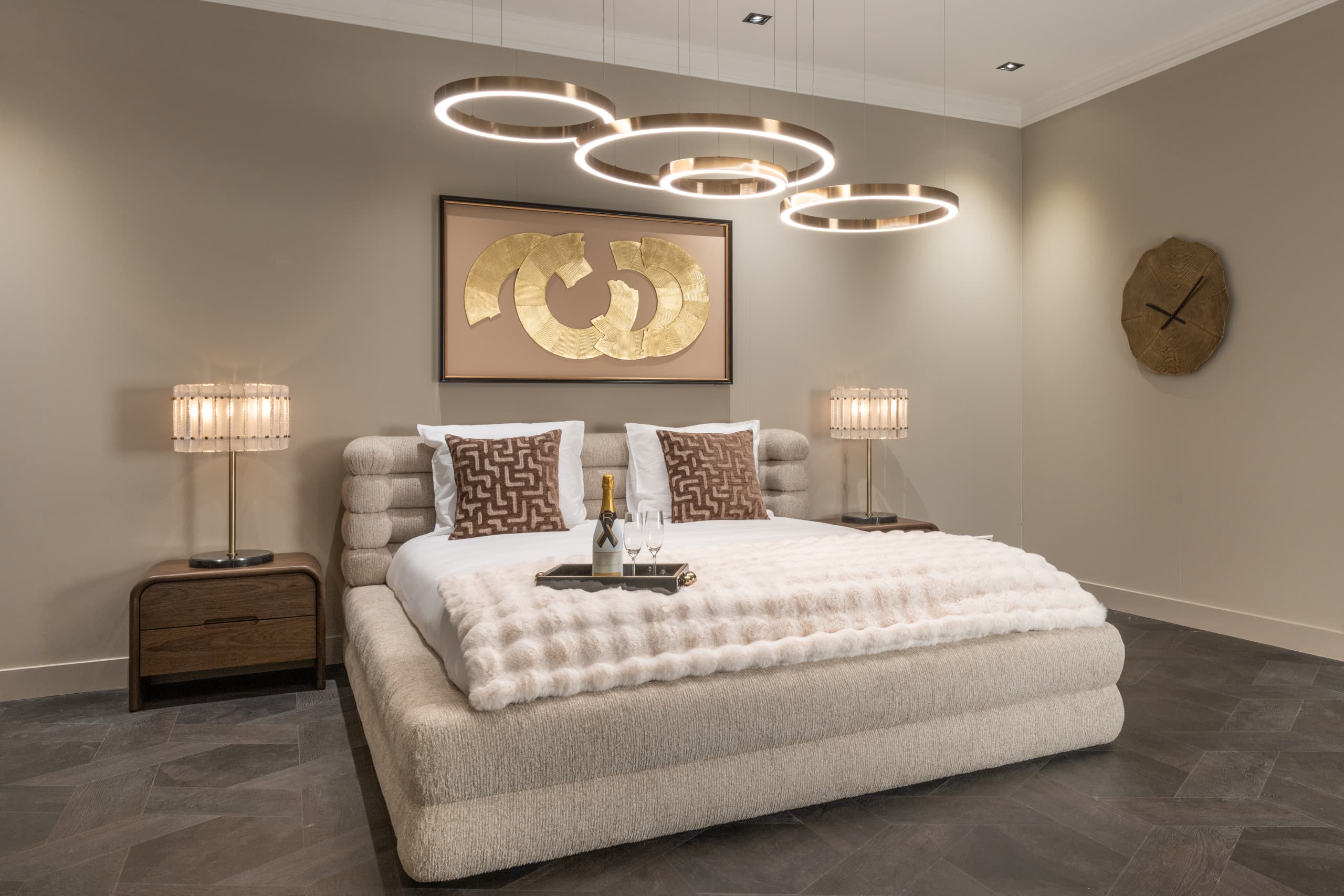 Opgemaakt bed met witte kussens, twee bruine sierkussens en een zachte plaid over het voeteneind, tussen twee nachtkastjes met tafellampen