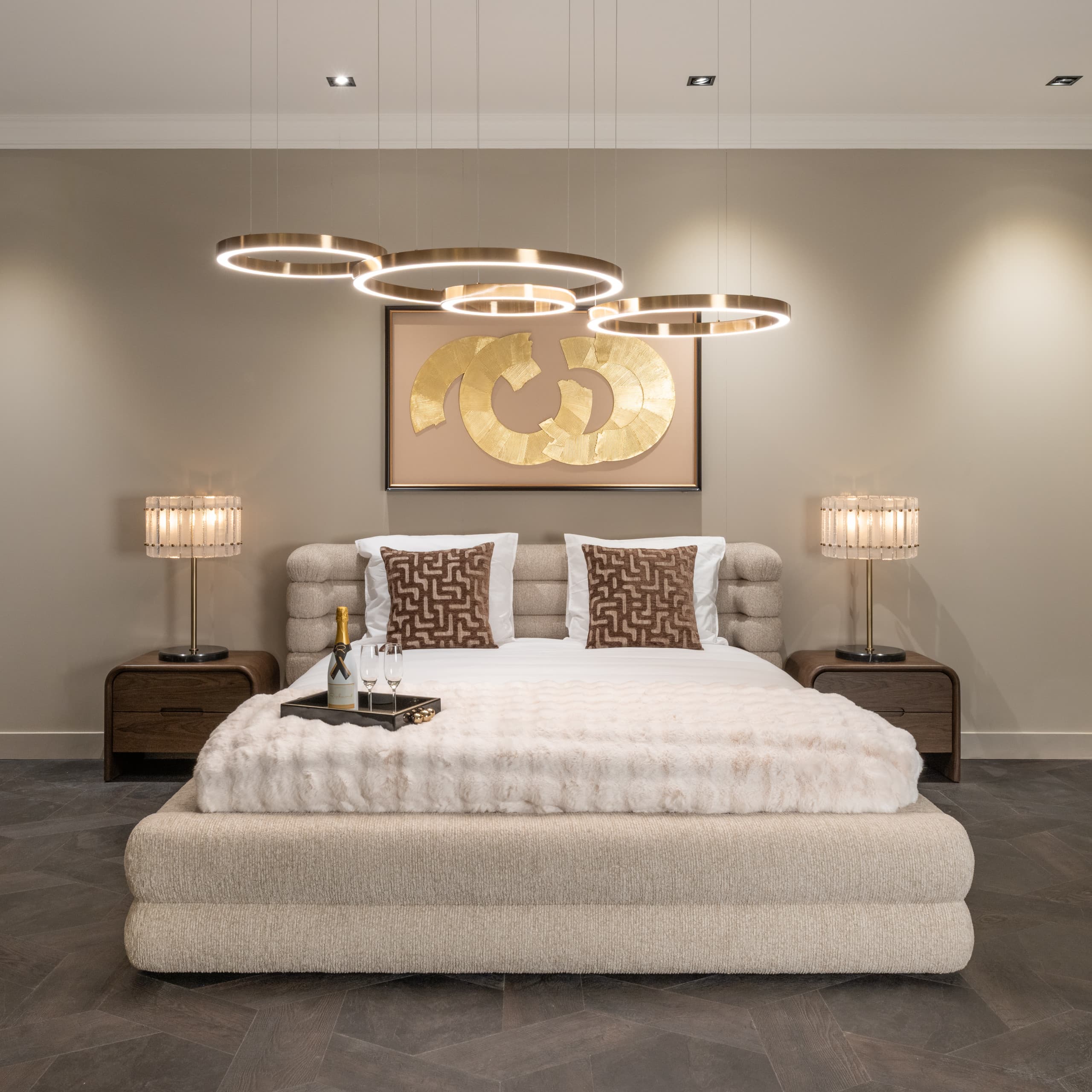 Slaapkamer met een gestoffeerd bed, twee brandende tafellampen op houten nachtkastjes en ringvormige hanglampen aan het plafond