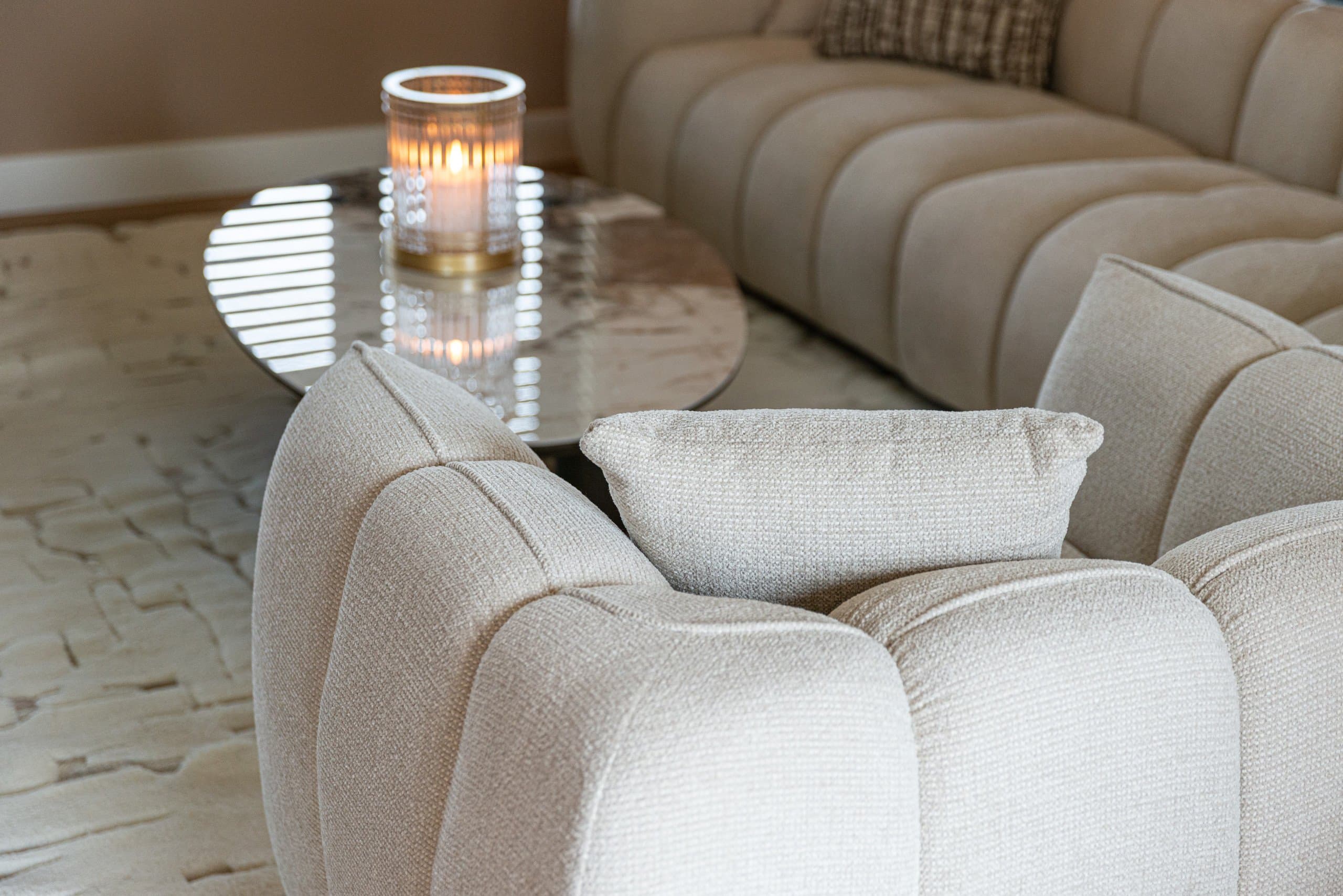 Zithoek met een crème bouclé bank en fauteuil, een ronde marmeren bijzettafel met brandend windlicht en een licht vloerkleed