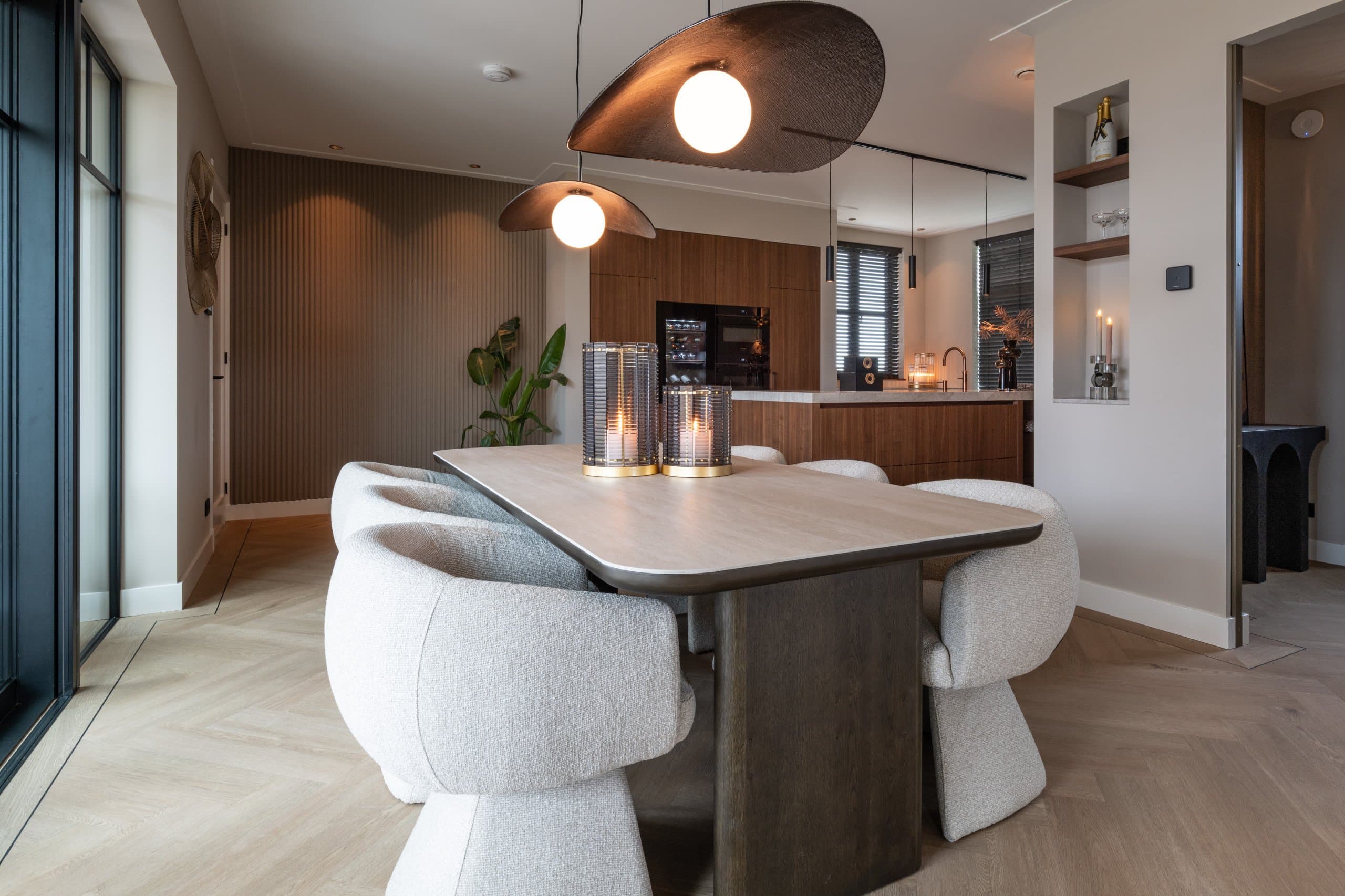 Eetkamer met een houten tafel, lichte bouclé stoelen, twee brandende windlichten en een open keuken met houten fronten op de achtergrond