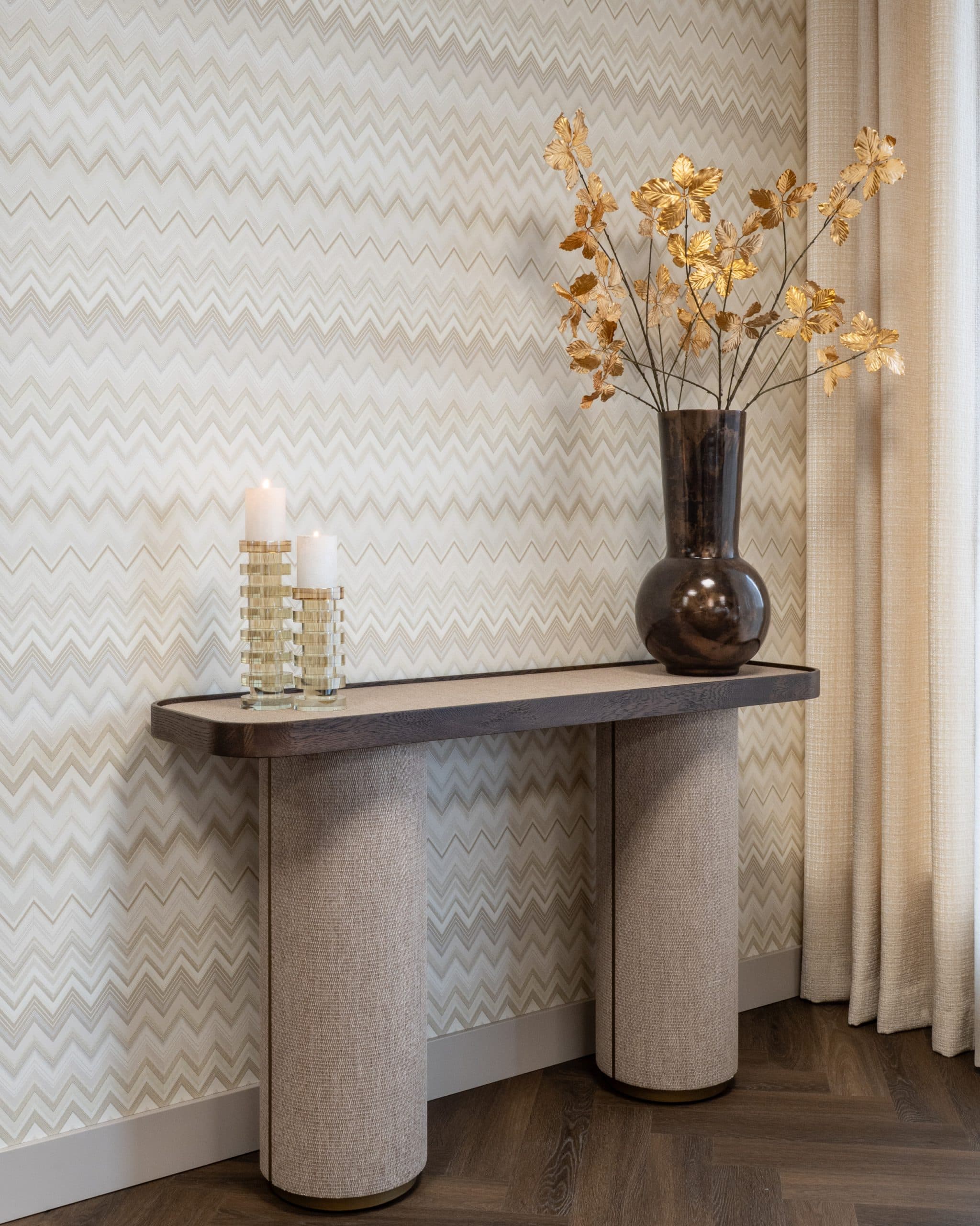 Smalle consoletafel met een donker eiken blad op twee met geweven linnen beklede poten, met twee kaarshouders en een bruine vaas met droogtakken ernaast