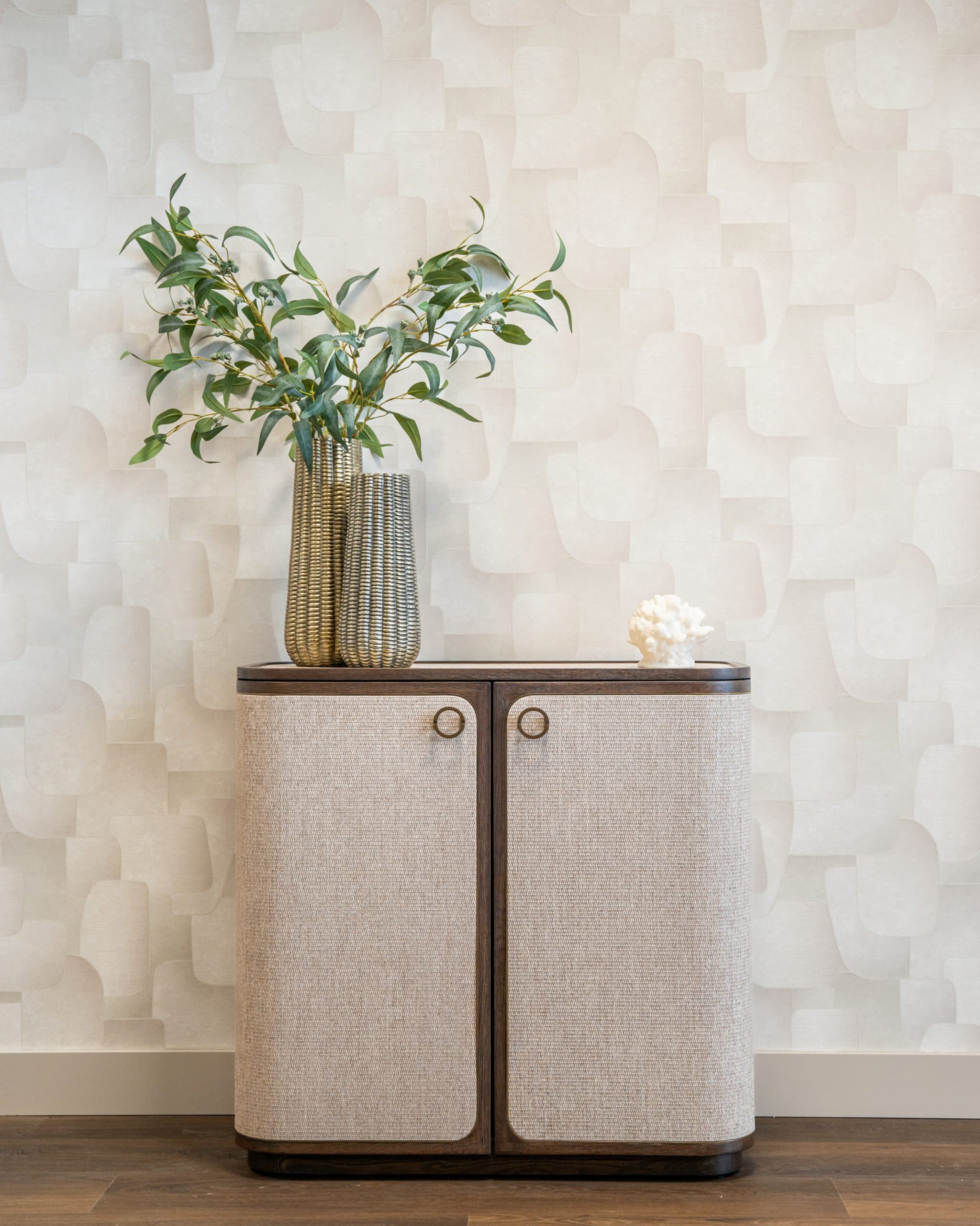 Beige dressoir met linnen deuren en donker houten blad, met twee goudkleurige vazen en een koraalobject erop