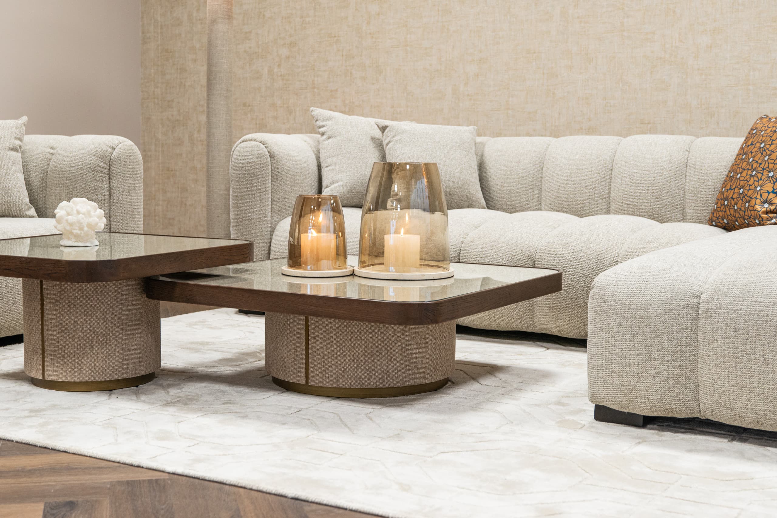 Lichte woonkamer met een grote crèmekleurige bank, twee houten salontafels met brandende kaarsen in amberkleurige windlichten en een licht vloerkleed