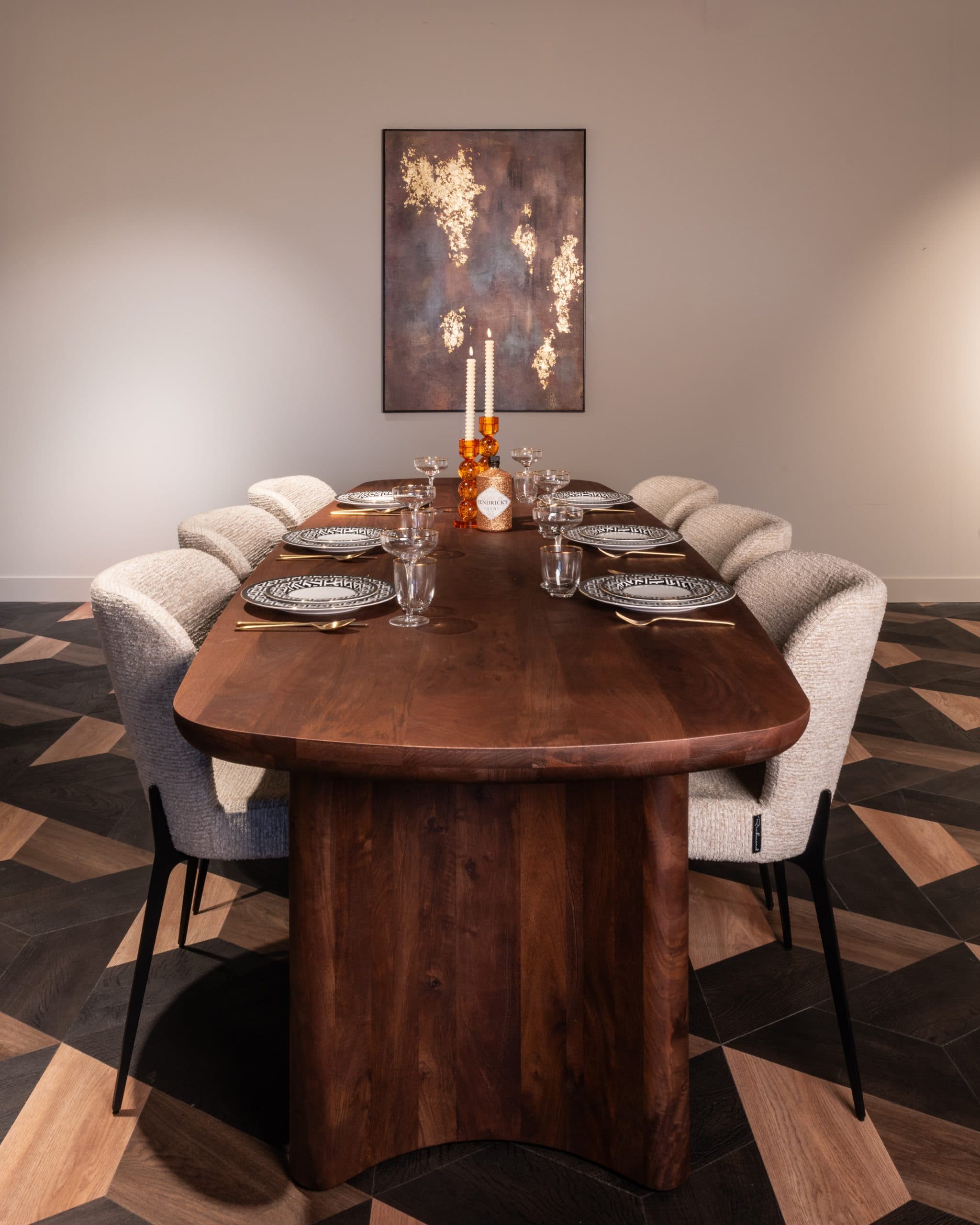 Grote houten eettafel met zichtbare nerf, gedekt met borden, glazen en kaarsen, omringd door bouclé stoelen op een visgraat houtvloer.