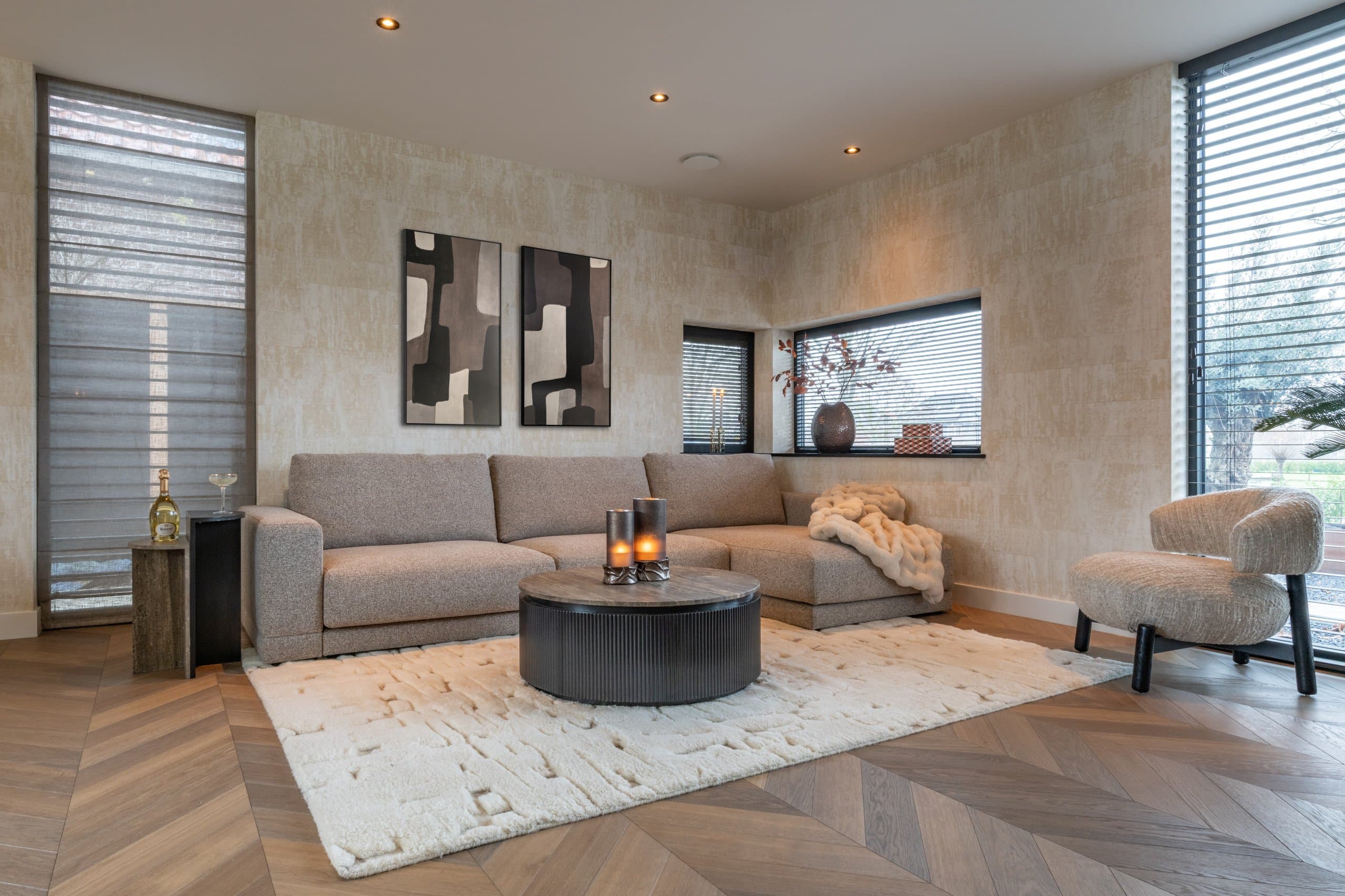 Woonkamer met beige hoekbank, ronde zwarte salontafel met brandende kaarsen en een wollig licht vloerkleed