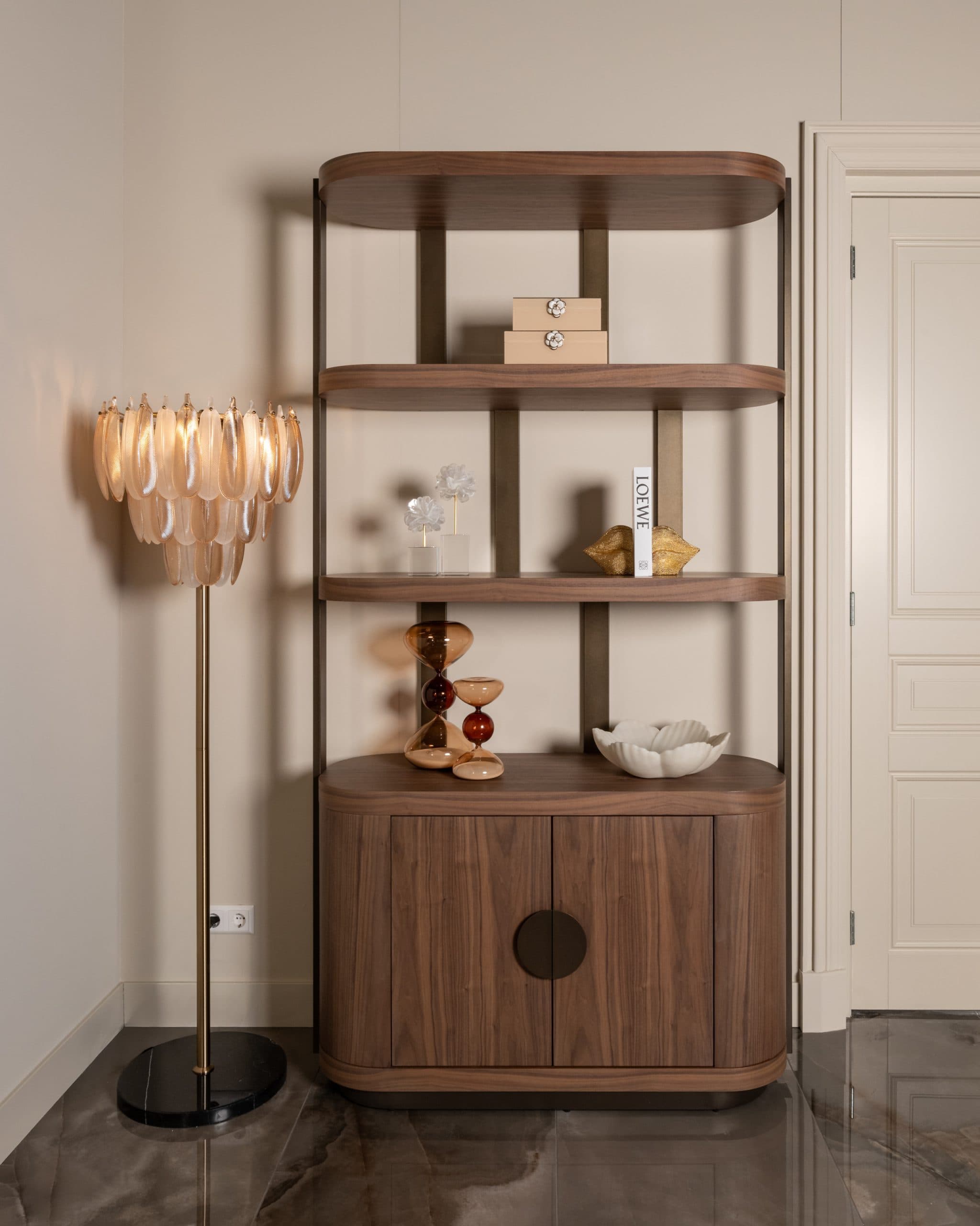 Open wandkast van walnoot met decoratie op de planken en een gesloten kastdeel onderin, naast een vloerlamp met schelpvormige kap