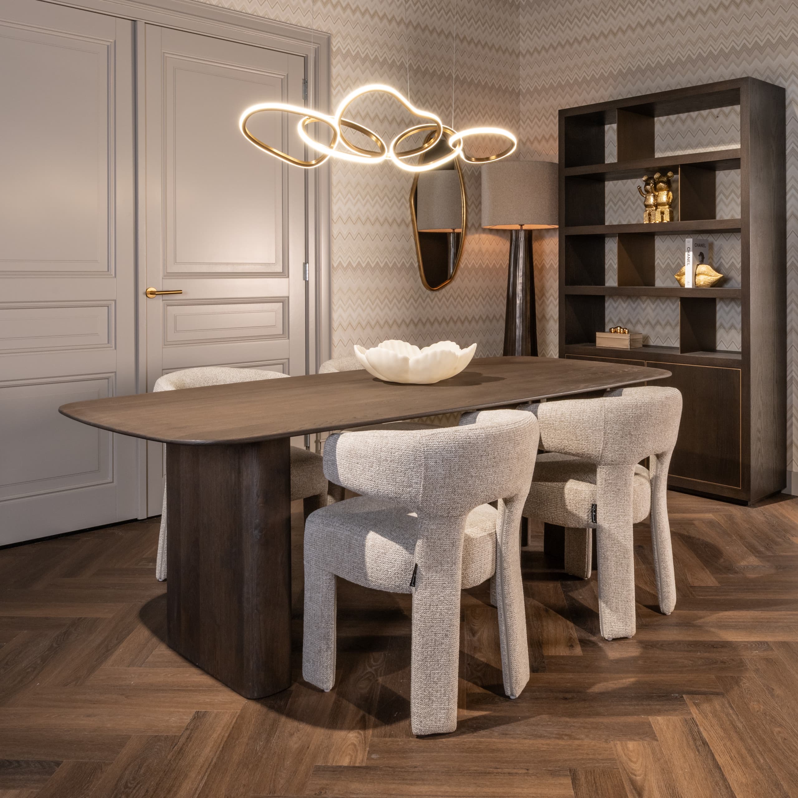 Eetkamer met een donkere houten eettafel, crèmekleurige bouclé stoelen en een witte schaal op tafel, op een visgraat parketvloer